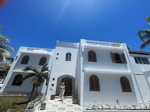 A white building with arched windows and a balcony, surrounded by palm trees.