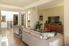 A modern living room with a sofa, a TV, and a dining area with a staircase.