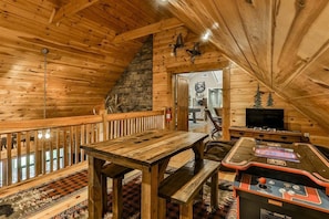 Un interior de madera con chimenea de piedra, una mesa de madera, un banco y una mesa de juegos.