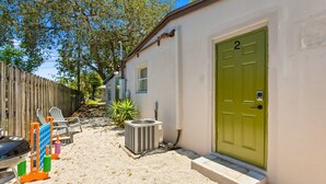 A small house with a green door, a barbecue grill, and outdoor seating.