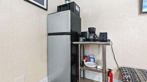 A compact kitchenette with a refrigerator, coffee maker, and a small shelf with kitchen essentials.