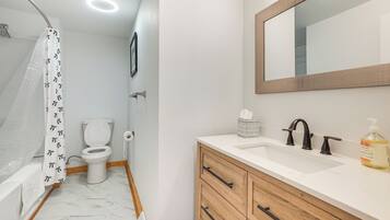A bathroom with a shower, toilet, sink, and wooden cabinets.