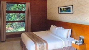 Une chambre d’hôtel avec un grand lit, une tête de lit en bois, une fenêtre avec des rideaux, un tableau accroché au mur et une table de chevet avec une lampe.