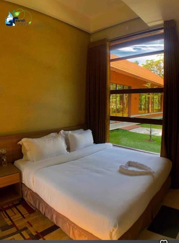 A hotel room with a large bed, a nightstand, a window with curtains, and a view of the outdoors.