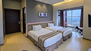 Une chambre d’hôtel avec deux lits, une grande fenêtre donnant sur un beau paysage, un luminaire au plafond et une porte.