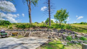 Un sitio arqueológico al aire libre con estructuras de piedra, un sendero de concreto y una carretilla.
