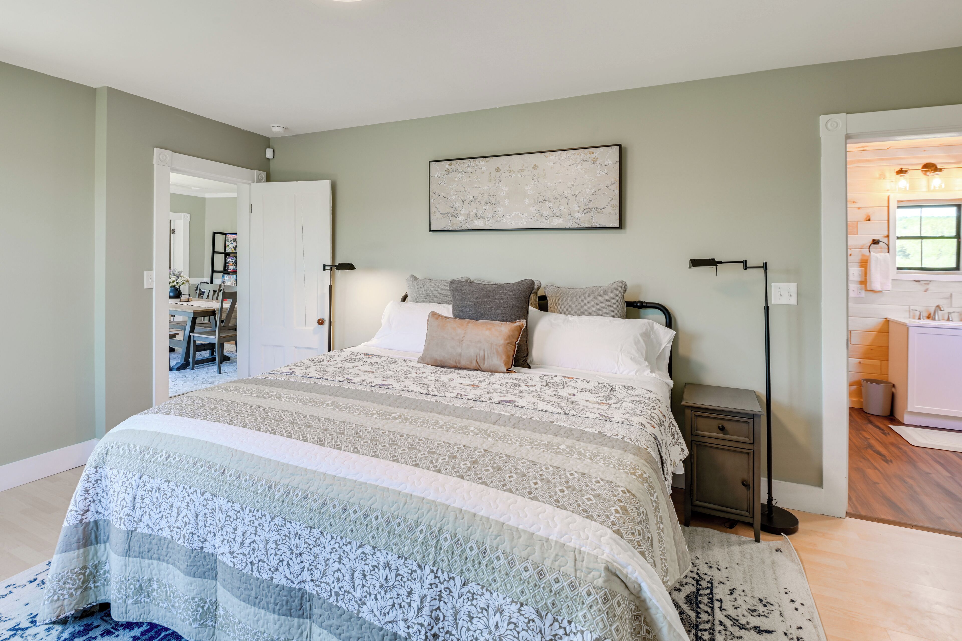 A bedroom with a large bed, bedside tables, a floor lamp, and a painting on the wall.