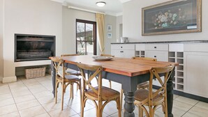 A dining area with a wooden table and chairs, a television, and a painting on the wall. - Winelands Golf Lodges 10 (Cape Town)