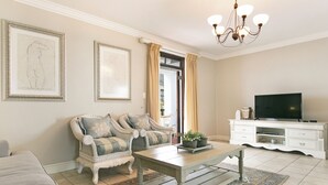 A living room with a sofa set, a coffee table, a TV, and a chandelier. - Winelands Golf Lodges 10 (Cape Town)
