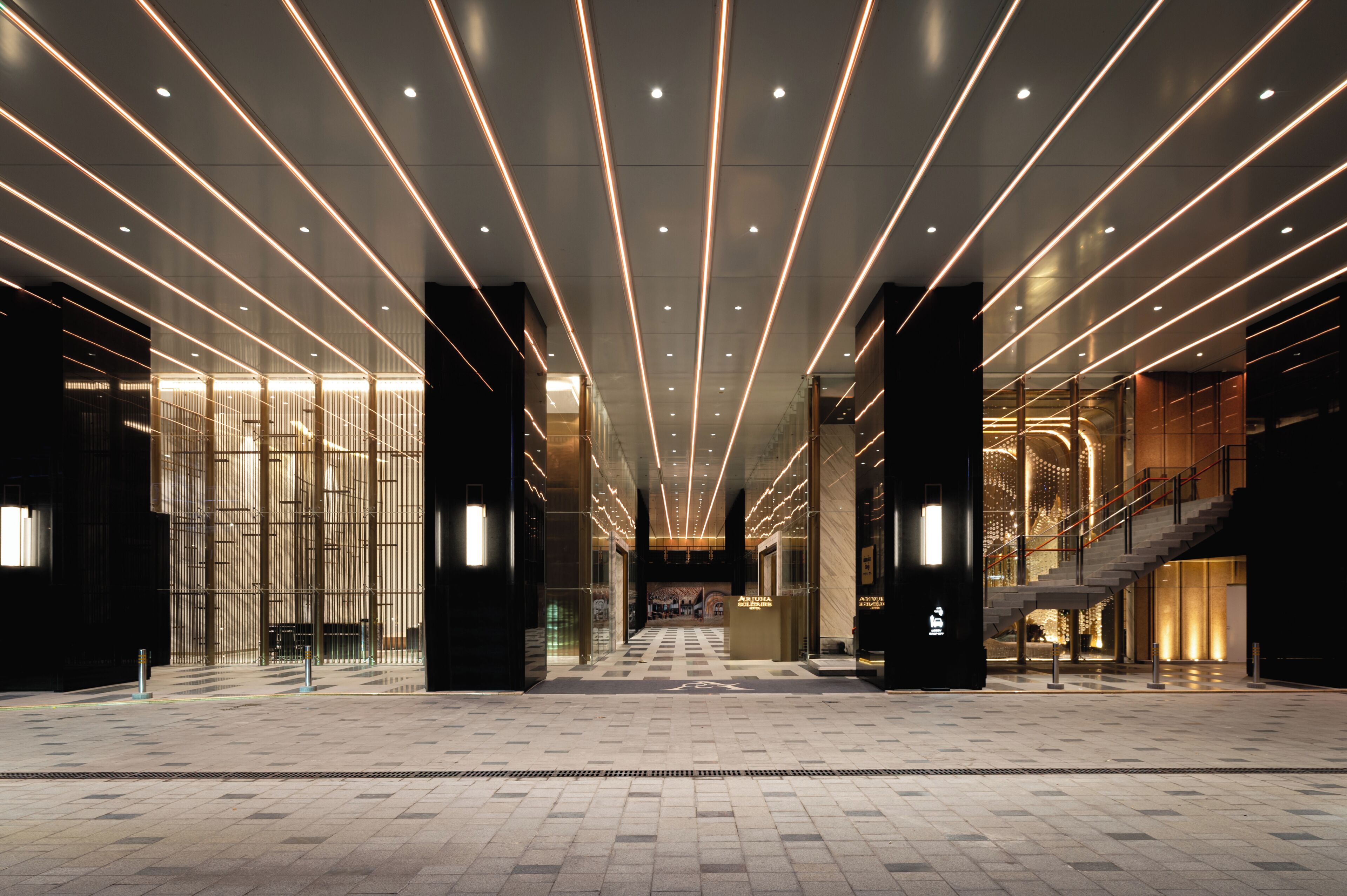 A spacious lobby with a modern design, featuring a central staircase and a series of illuminated lines on the ceiling.