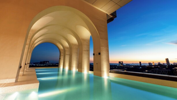 An infinity pool with a city view, under a covered area with arches.