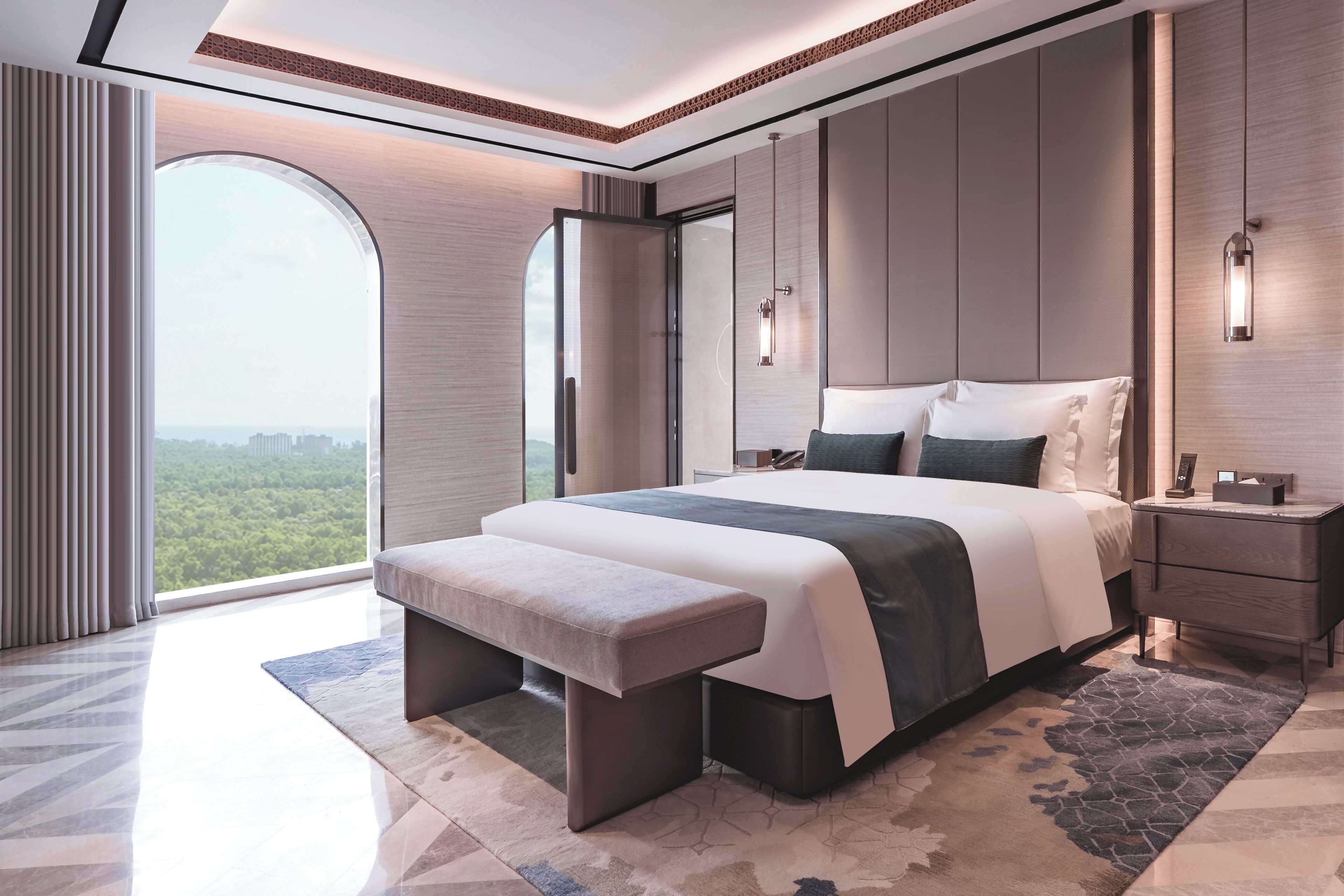 A modern bedroom with a large bed, bedside tables, a bench, and a view of greenery.