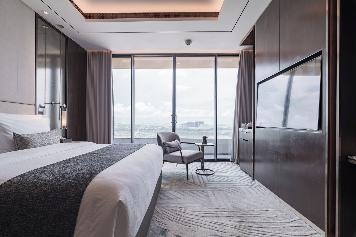 A modern hotel room with a large bed, a chair, a small table, and a TV.