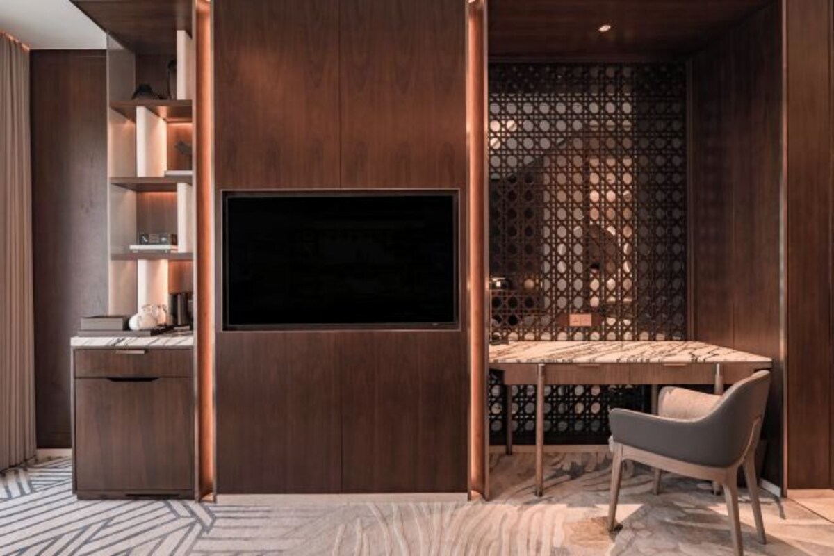 A modern room with a flat-screen TV mounted on a wooden wall, a dining table with chairs, and a decorative partition with a geometric pattern.