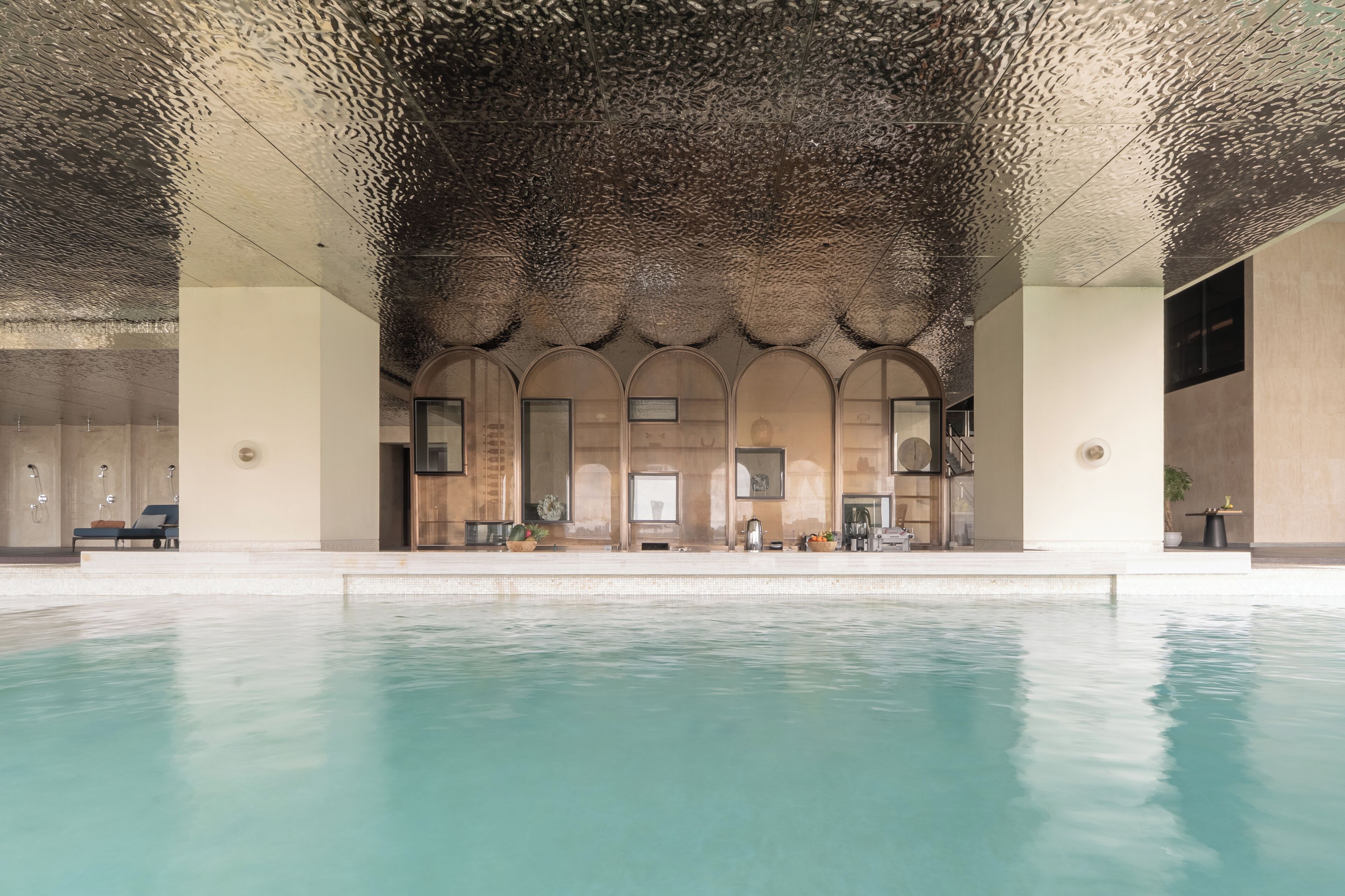 Un espace piscine doté d’un plafond orné d’un motif texturé original, d’un coin salon avec des fauteuils confortables et d’une vue dégagée sur la piscine.