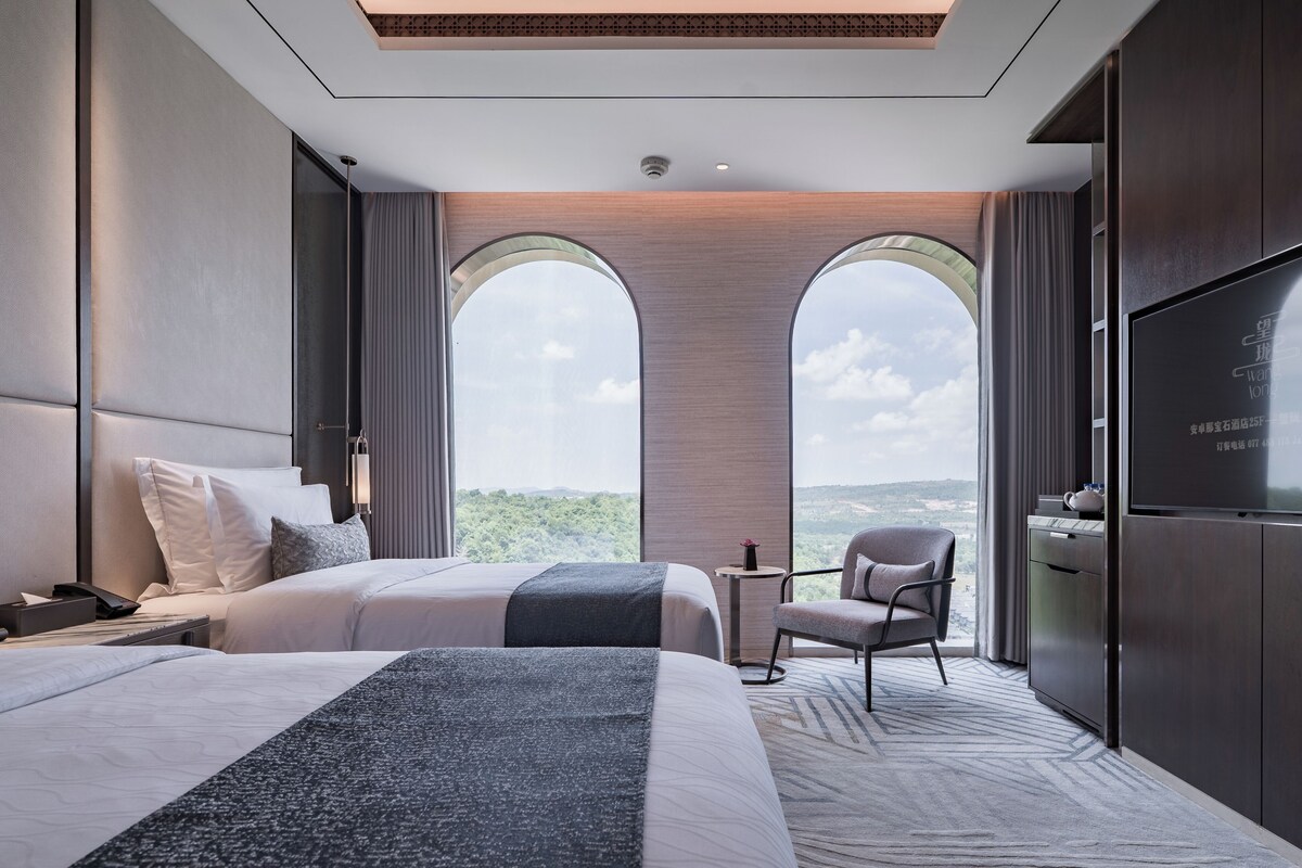 A modern hotel room with two beds, a TV, a small table, and a chair.