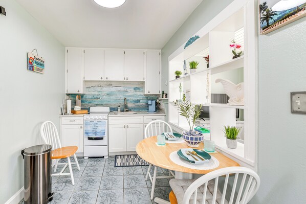 Une cuisine compacte avec des meubles blancs, une table à manger en bois et une petite fenêtre agrémentée de plantes.