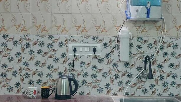 Een keuken met turquoise wanden, een betegelde spatwand, een spoelbak, een waterkoker en een waterdispenser.