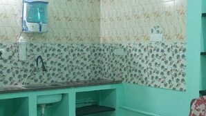 Een kamer met turquoise wanden, een decoratieve spatwand, een plafondventilator, een waterdispenser en een houten stoel.