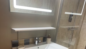 A modern bathroom with a white vanity, a glass shower enclosure, and a mirror above the sink. - Room "Abricot (Uzès)