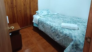 Una habitación pequeña con cama individual, paneles de madera en una pared y suelo de baldosas.