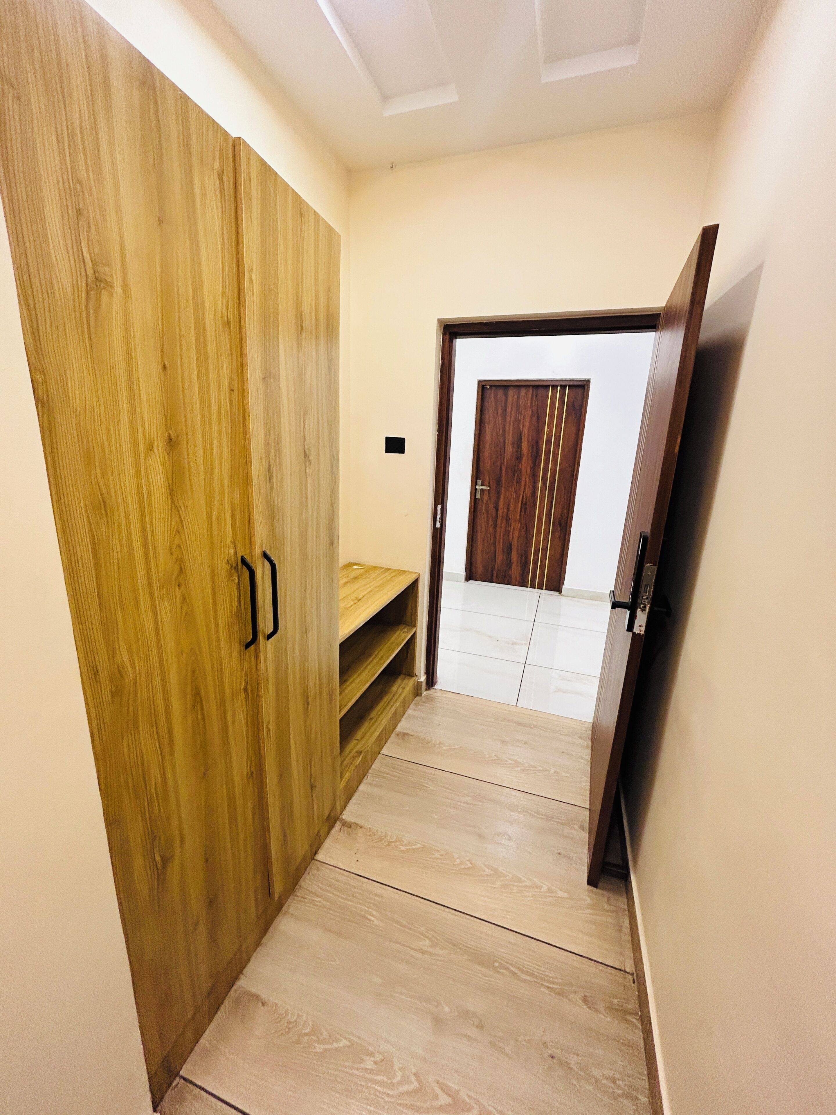 A hallway with a wooden wardrobe, a small shelf, and a door leading to another room.