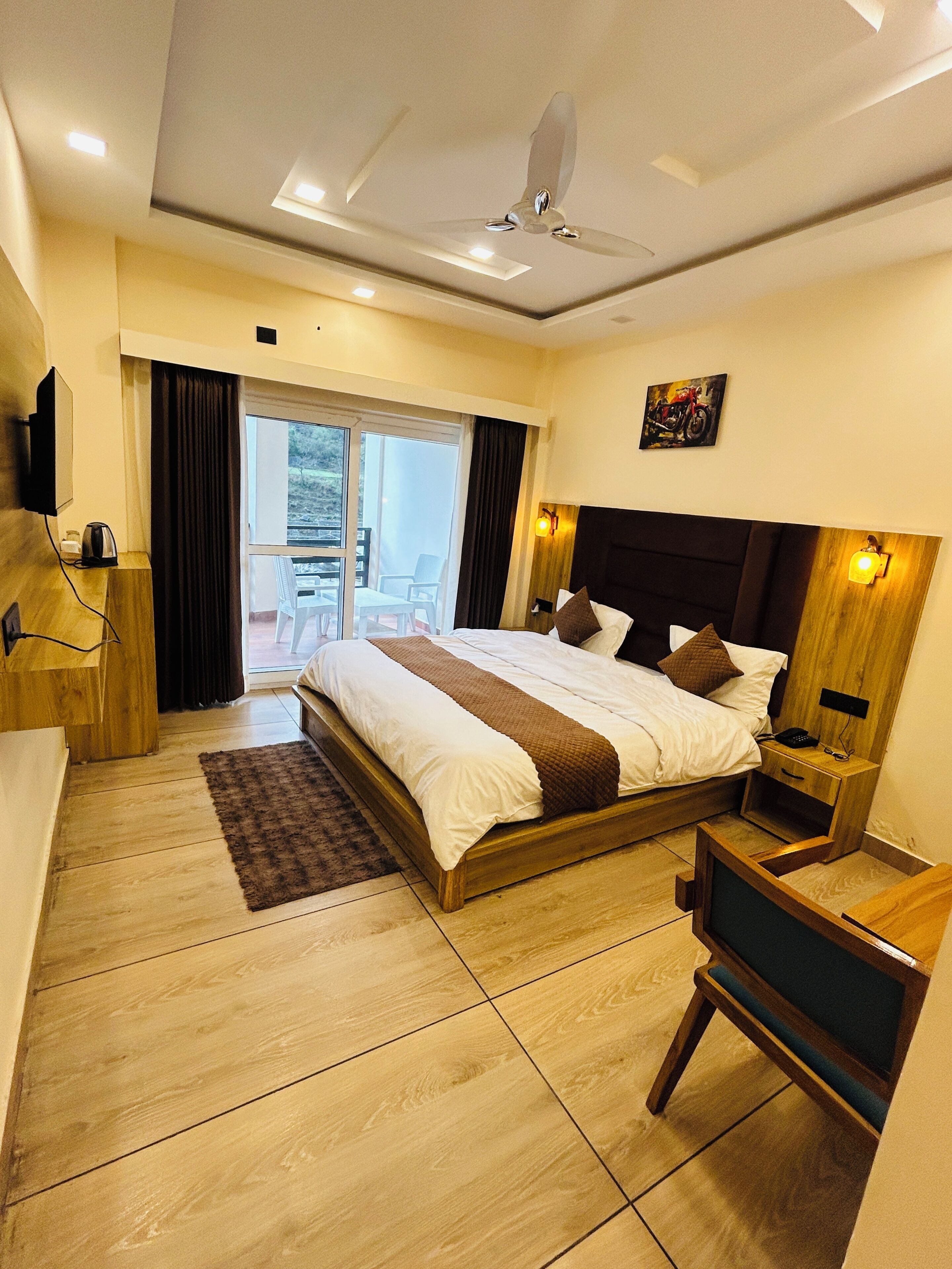 A hotel room with a bed, bedside table, TV, and a view of the outdoors.
