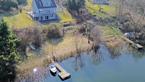 Una casa con un muelle que se adentra en el agua, rodeada de árboles y un área con césped.