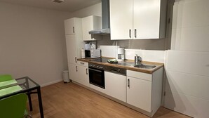 Cocina compacta con armarios blancos, microondas, cafetera y lavabo.