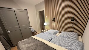 Un dormitorio con cama, armario, silla, mesita de noche y lámpara.