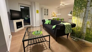 Una sala de estar con sofá, mesa de centro, televisor y una pared decorada con un diseño de hojas verdes.