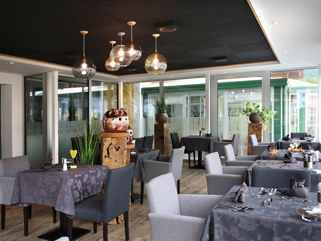 Un restaurante con varias mesas y sillas, ventanas amplias y lámparas colgantes.