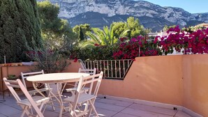 Eine Terrasse mit Tisch und Stühlen, umgeben von Pflanzen und Blumen, mit Blick auf die Berge im Hintergrund.