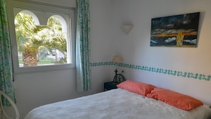 Ein Schlafzimmer mit Bett, einem Fenster mit Vorhängen, einer Wandleuchte, einem Gemälde und einer Zierleiste.