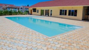 A swimming pool with a tiled deck, a building with a red roof, and a clear blue sky. - Sanay cozy home (Eldoret)
