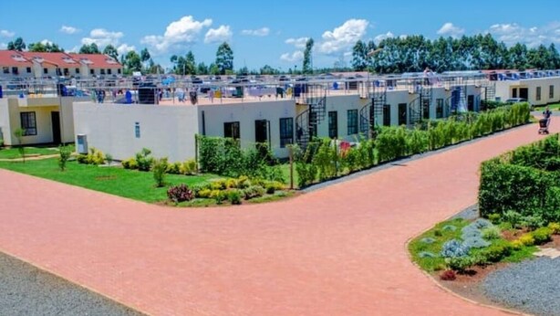 A series of white buildings with external staircases, a paved walkway, and landscaped areas with shrubs and small trees. - Sanay cozy home (Eldoret)