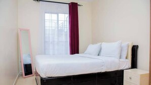 A bedroom with a black bed frame, white bedding, a mirror, and a window with a red curtain. - Sanay cozy home (Eldoret)