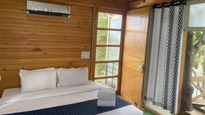 A wooden cabin room with a bed, a ceiling fan, and a window with a view of greenery. - Okho Resort Kalka Panchkula (Kalka)