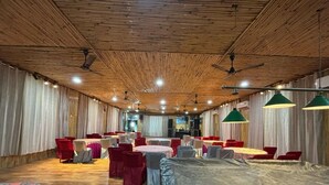 A banquet hall with round tables, red and grey chairs, and a stage area. - Okho Resort Kalka Panchkula (Kalka)