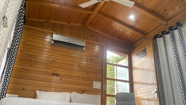 A wooden-paneled room with a bed, a chair, and a ceiling fan. - Okho Resort Kalka Panchkula (Kalka)