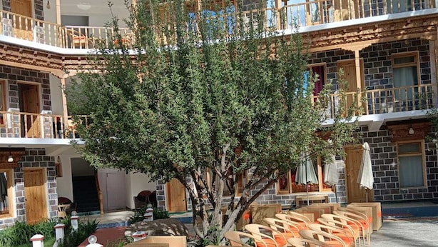 Un patio con mobiliario exterior, un árbol central y un edificio con balcones.