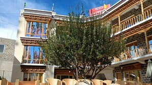 Un hotel de estilo arquitectónico tradicional, con un balcón que tiene mobiliario de mimbre y un árbol en el centro.