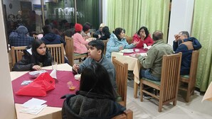 Un comedor con mesas y sillas de madera, un mantel rojo y una cortina verde al fondo.