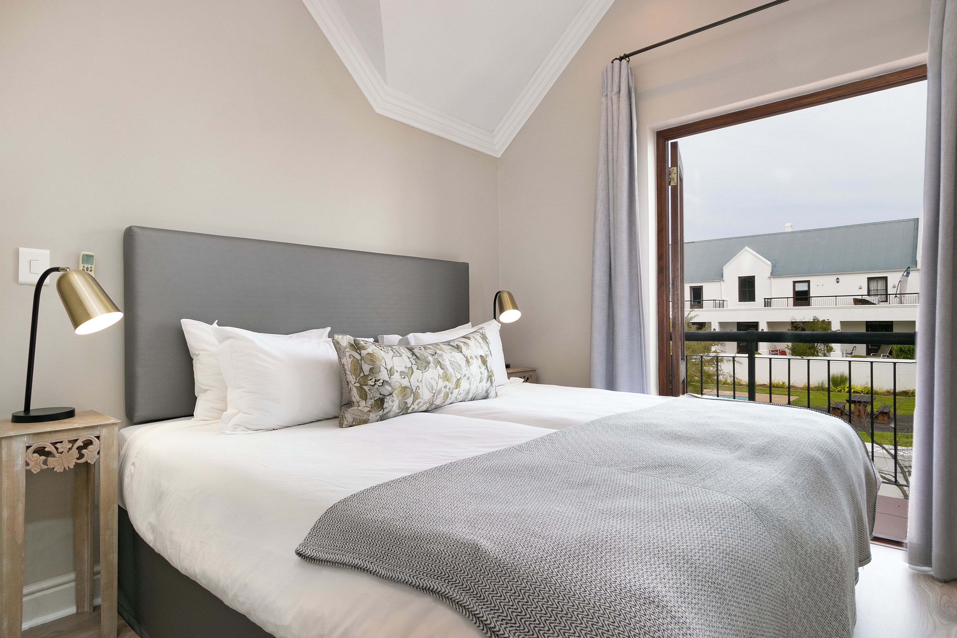 Ein Schlafzimmer mit einem großen Bett, zwei Nachttischlampen und Blick auf ein Gebäude durch ein Fenster.