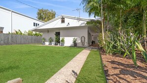 Une maison moderne avec une pelouse bien entretenue, un chemin de gravier et diverses plantes en pot.