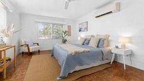 Une chambre à coucher comprenant un lit, une chaise, une table de chevet, une lampe et une fenêtre avec des stores.