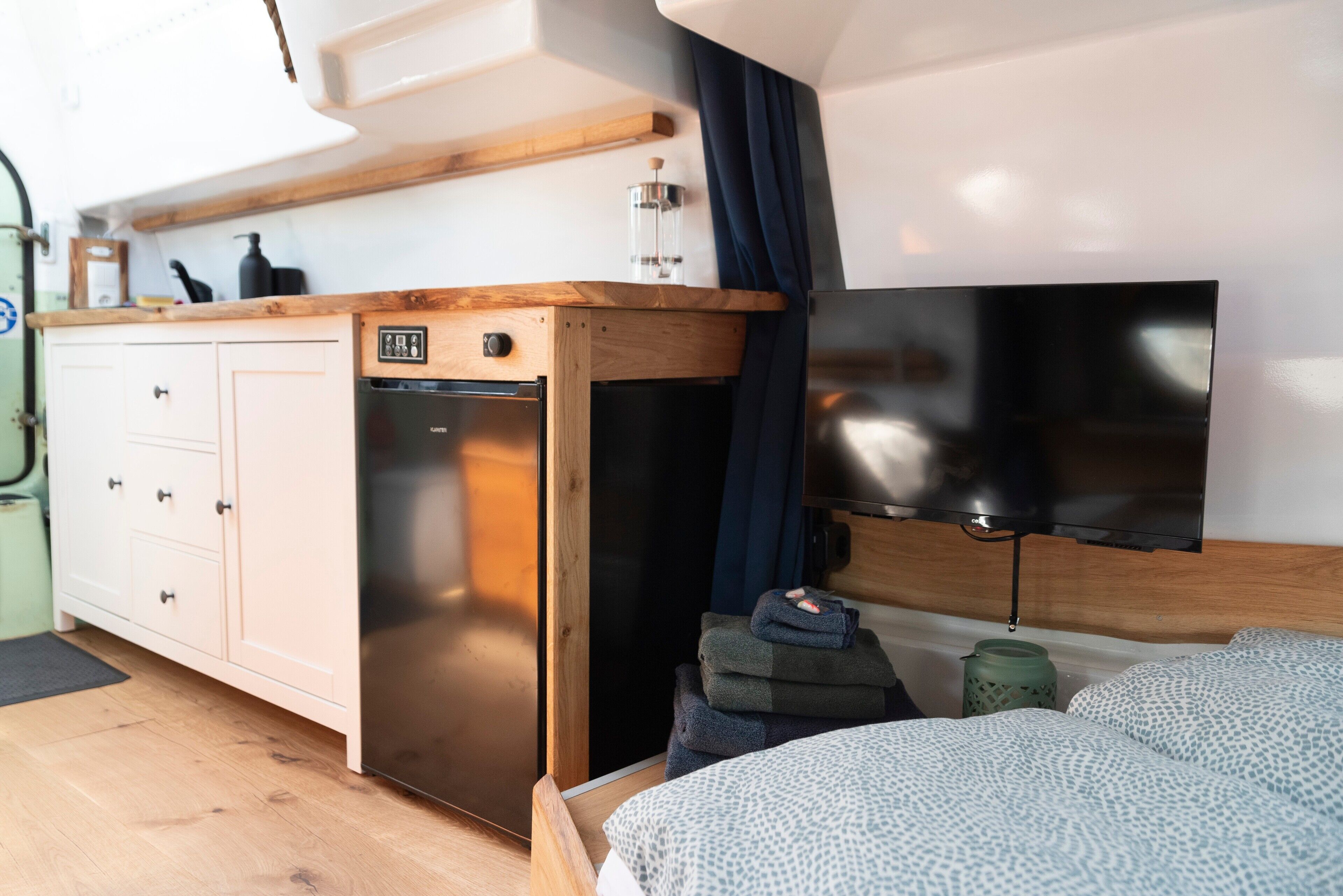 Una camera compatta con un letto, un angolo cottura, una TV e una finestra con tende.