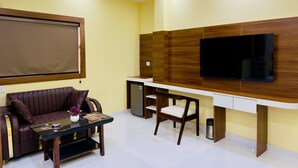 A modern living room with a sofa, a coffee table, a TV mounted on a wooden wall, and a desk with a chair. - HOTEL ROSHAN (Varanasi)