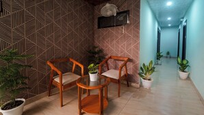 A hallway with patterned wallpaper, a wooden chair, a glass table, and potted plants. - HOTEL ROSHAN (Varanasi)