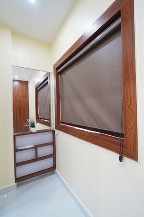 Une pièce avec une grande fenêtre, un miroir, une armoire en bois et une petite étagère sur laquelle est posée une plante.